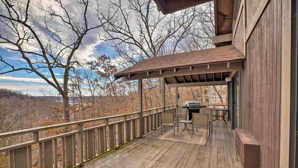 A wooden deck with a grill and seating area, overlooking a forested landscape.