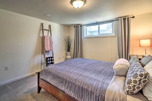 Ein Schlafzimmer mit Bett, einer Leiter, einem Fenster mit Vorhängen, einer Pflanze und einer Lampe.
