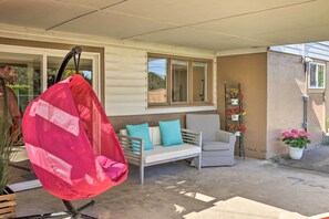 Eine überdachte Terrasse mit einem weißen Sofa, einem gestreiften Sessel und einem Hängesessel.