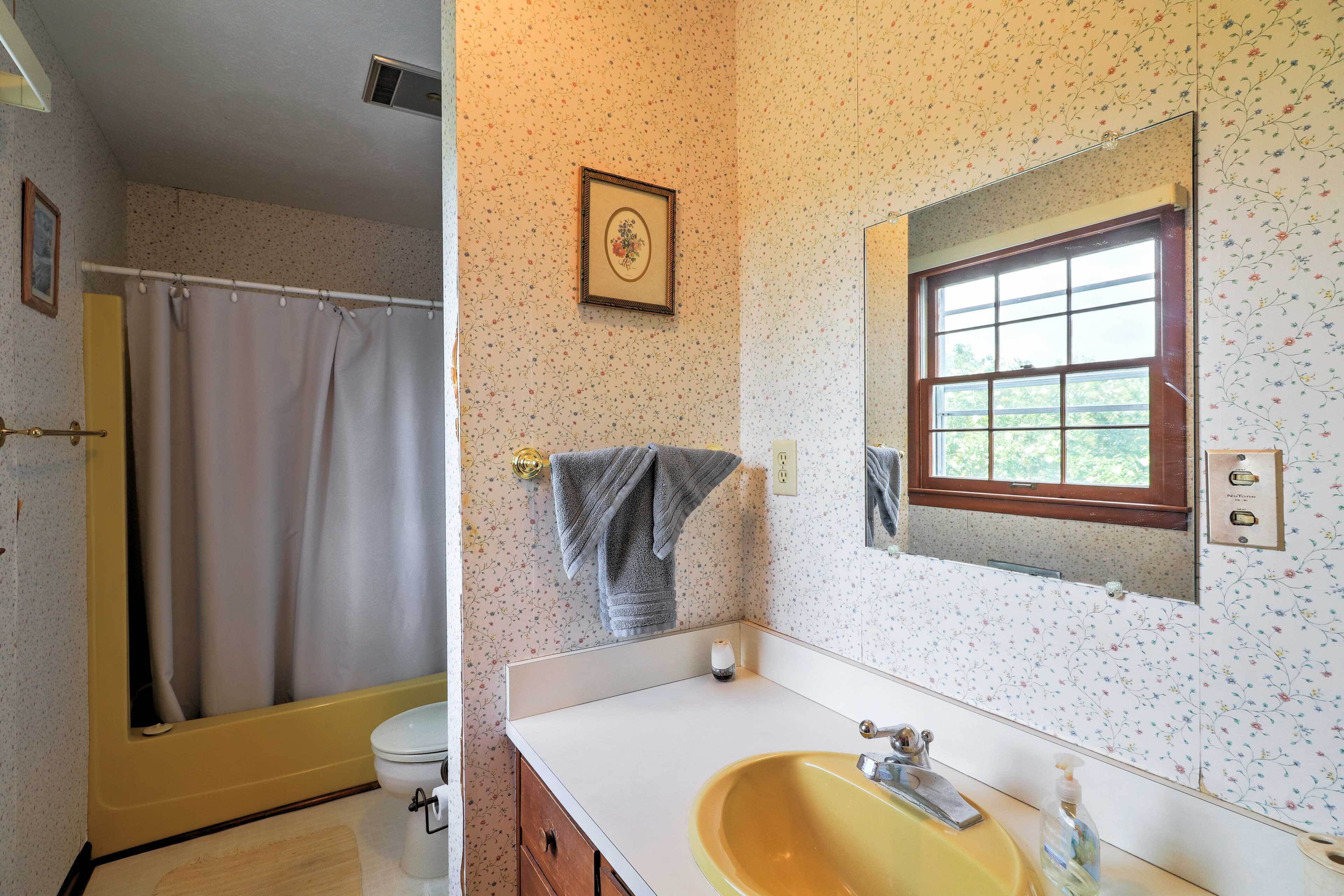 A bathroom with a shower, toilet, sink, and a window.