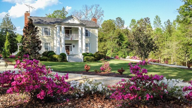 A two-story house with a front porch, surrounded by a well-maintained lawn and flowering bushes. - Historic 1840's Estate on 20 Acres w/ Guest House (Lafayette)