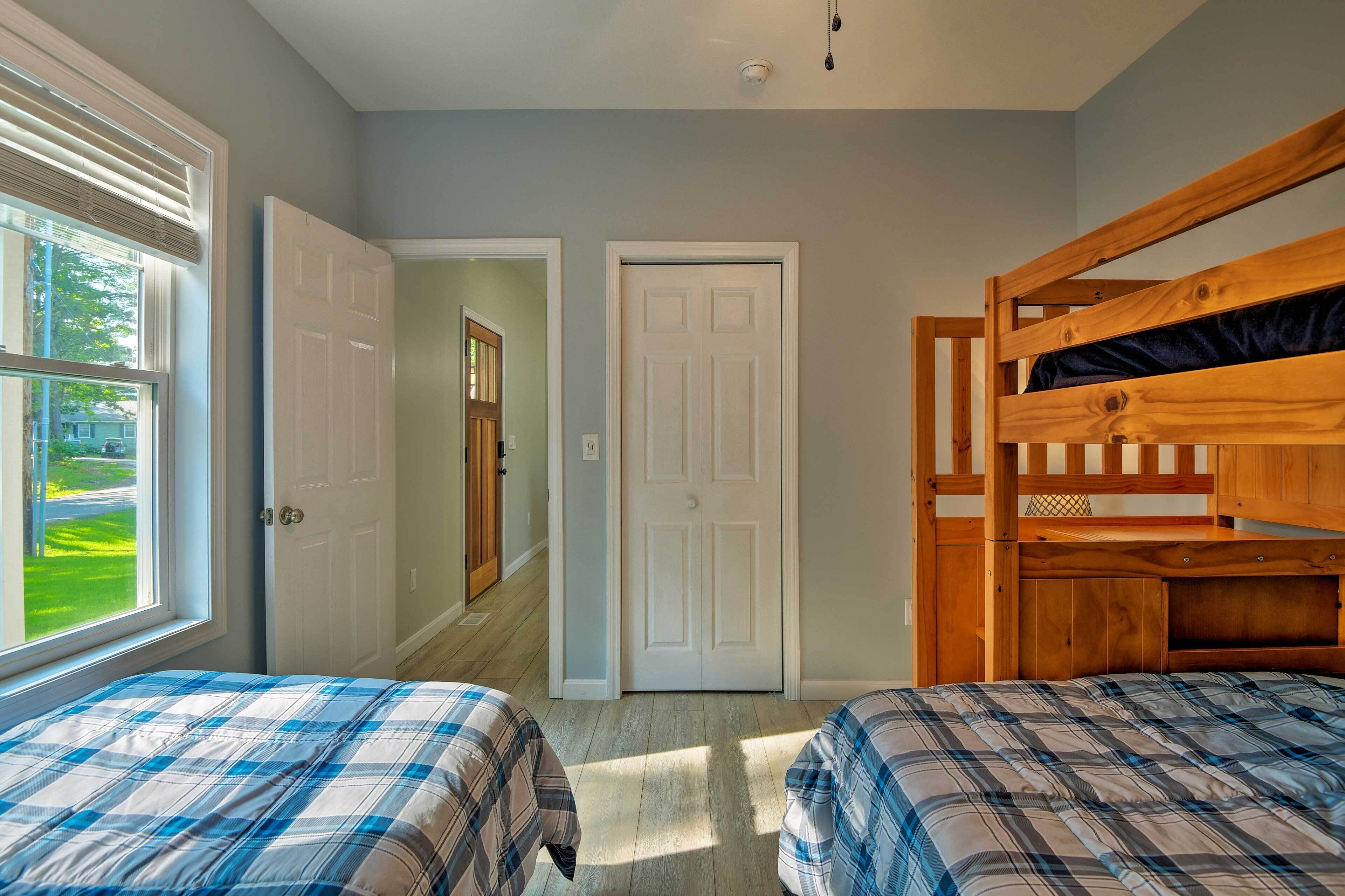 A bedroom with two beds, a wooden bunk bed, a large window, and a door leading to another room.