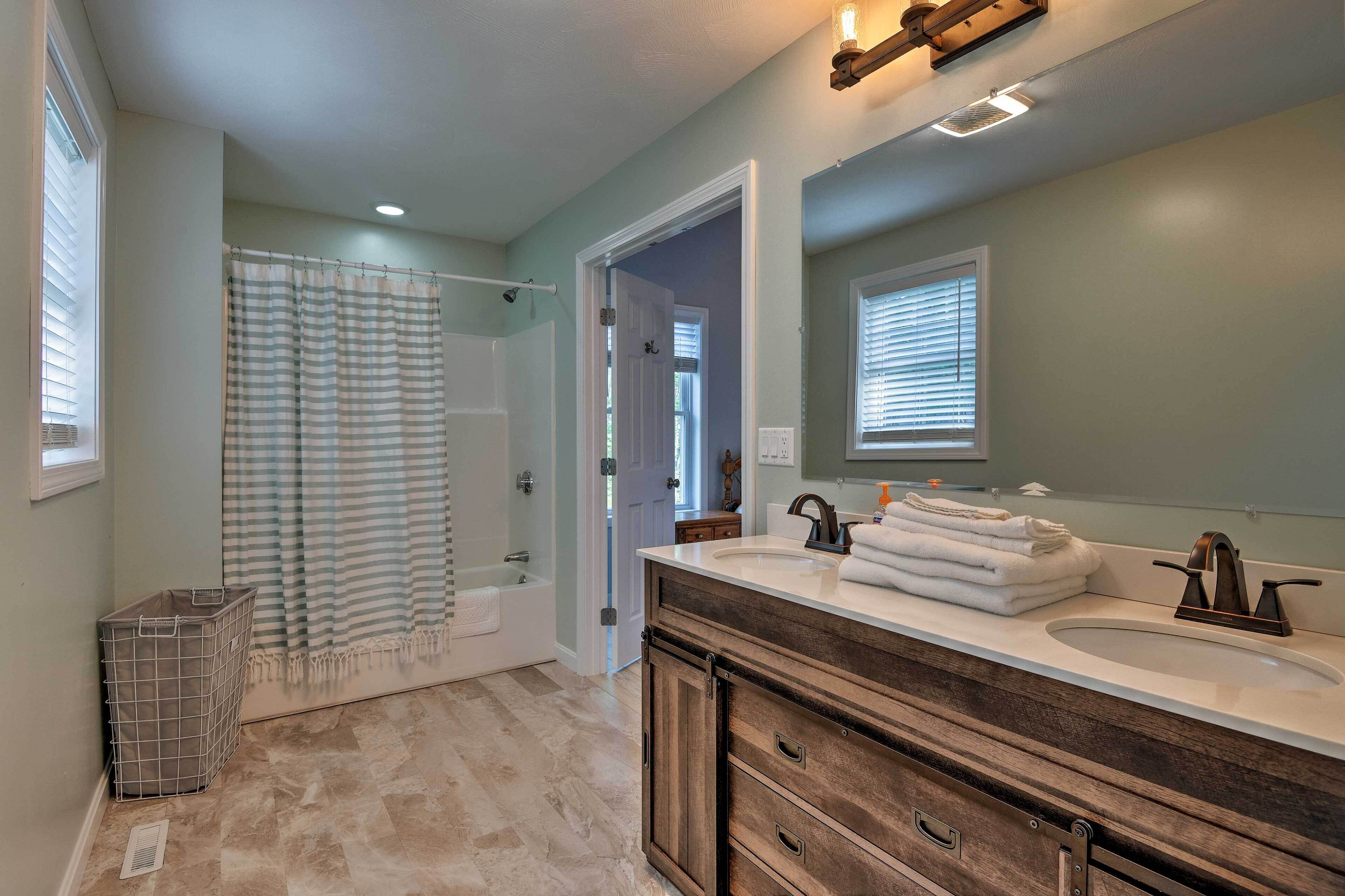 A bathroom with a double sink vanity, a shower with a striped curtain, and a walk-in closet.