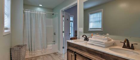 A bathroom with a double sink vanity, a shower with a striped curtain, and a walk-in closet.