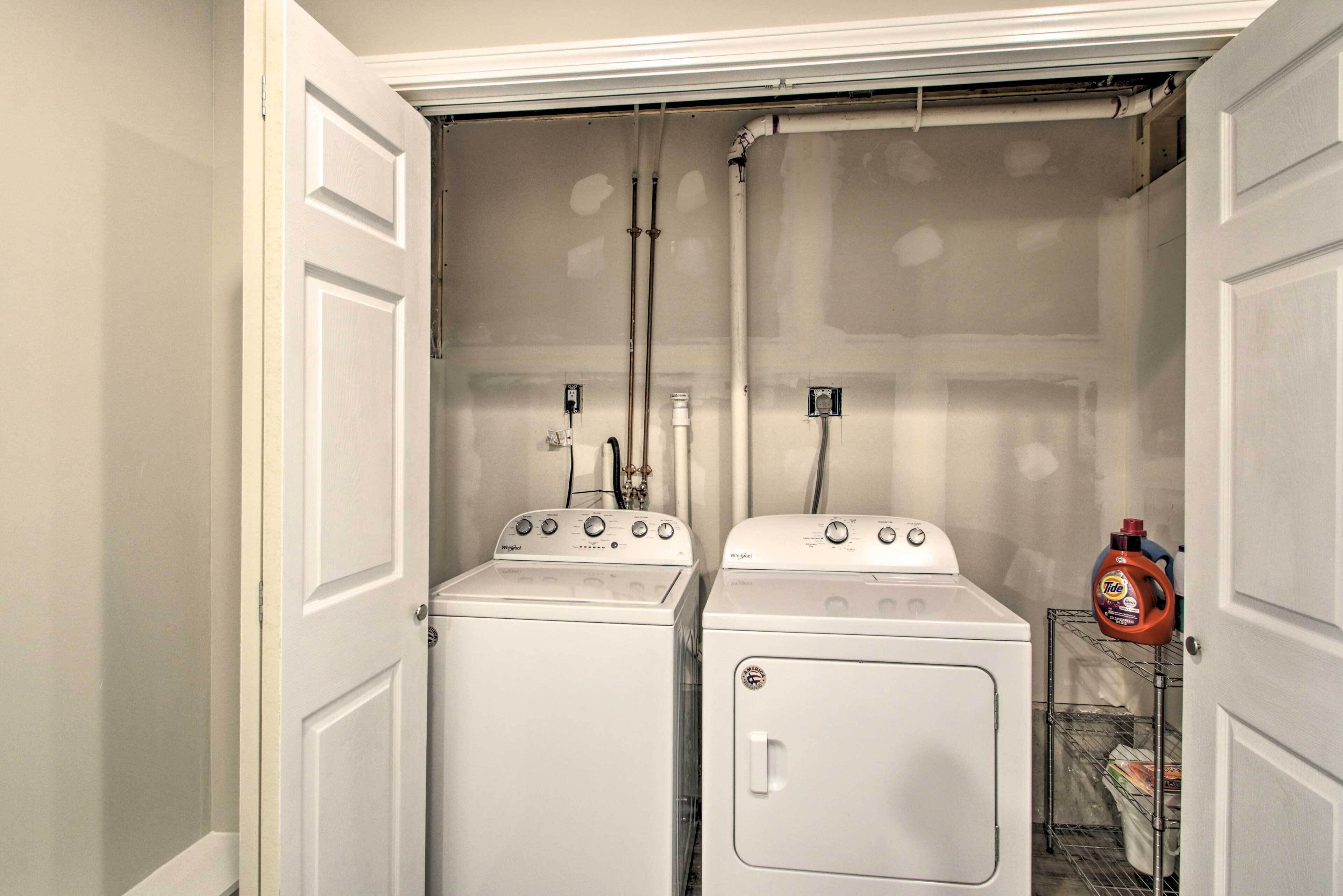 A laundry room with two stacked washers and dryers, a metal rack with laundry, and a bottle of Tide detergent.