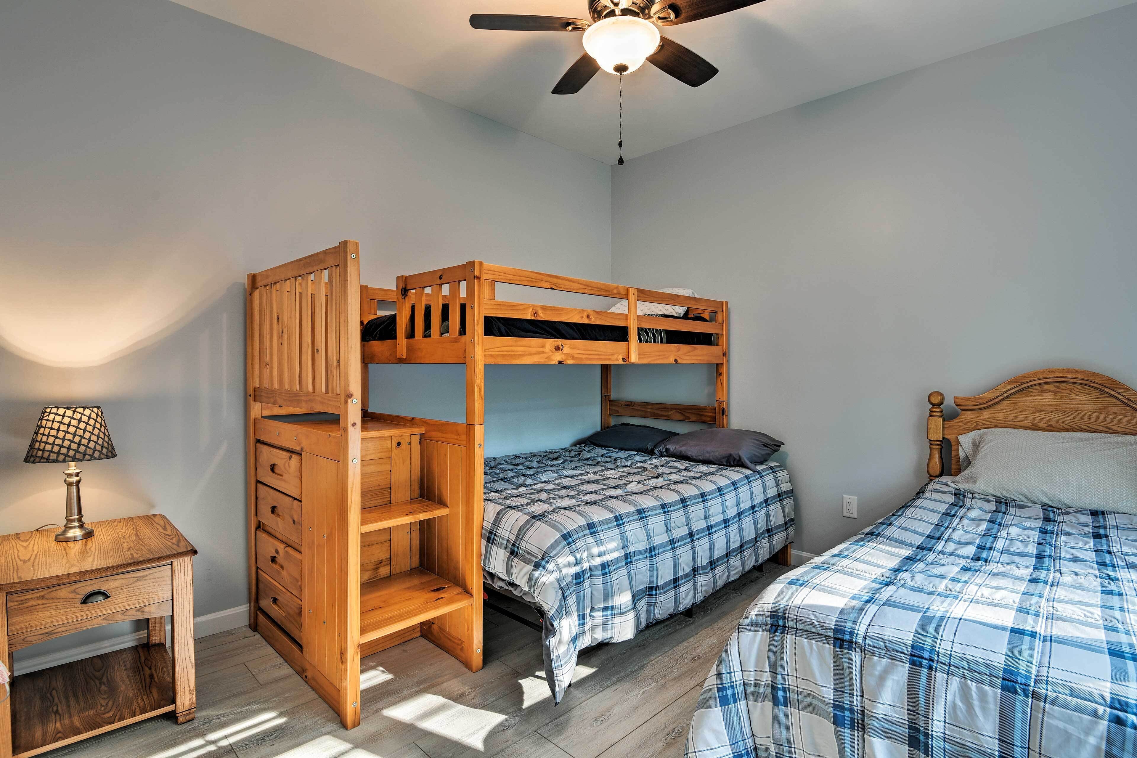 A bunk bed room with a ceiling fan, a desk with a lamp, and a bed with a plaid bedspread.