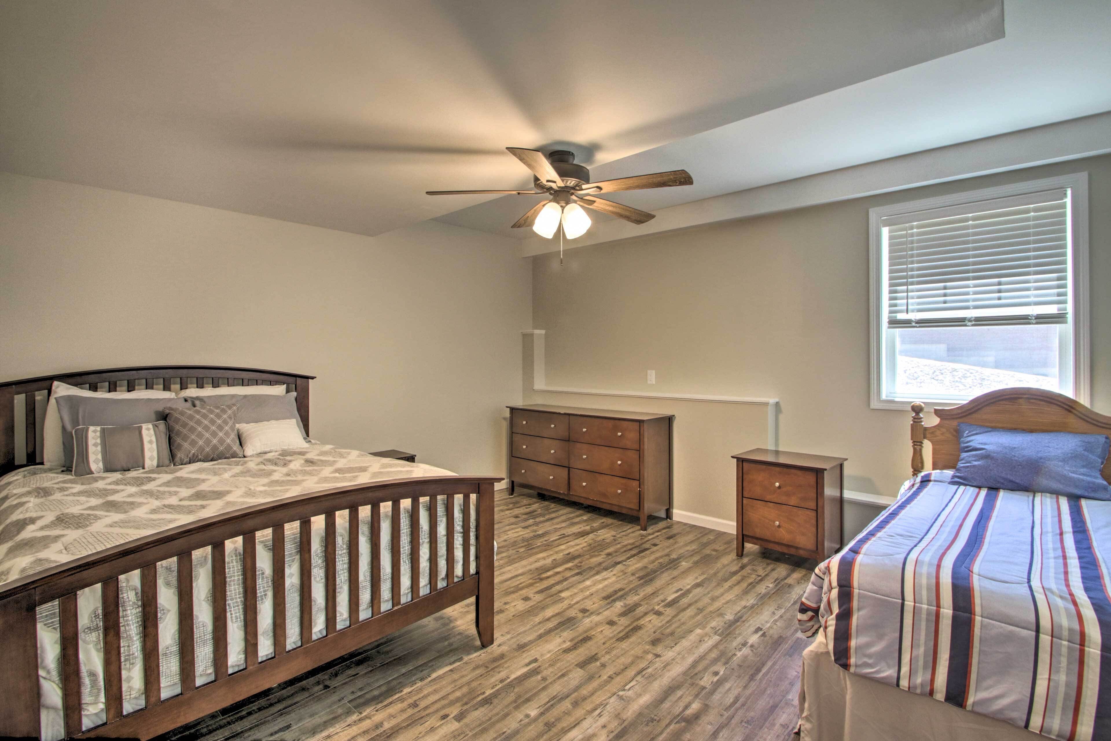 A bedroom with two beds, a wooden floor, a ceiling fan, a dresser, and a window with blinds.