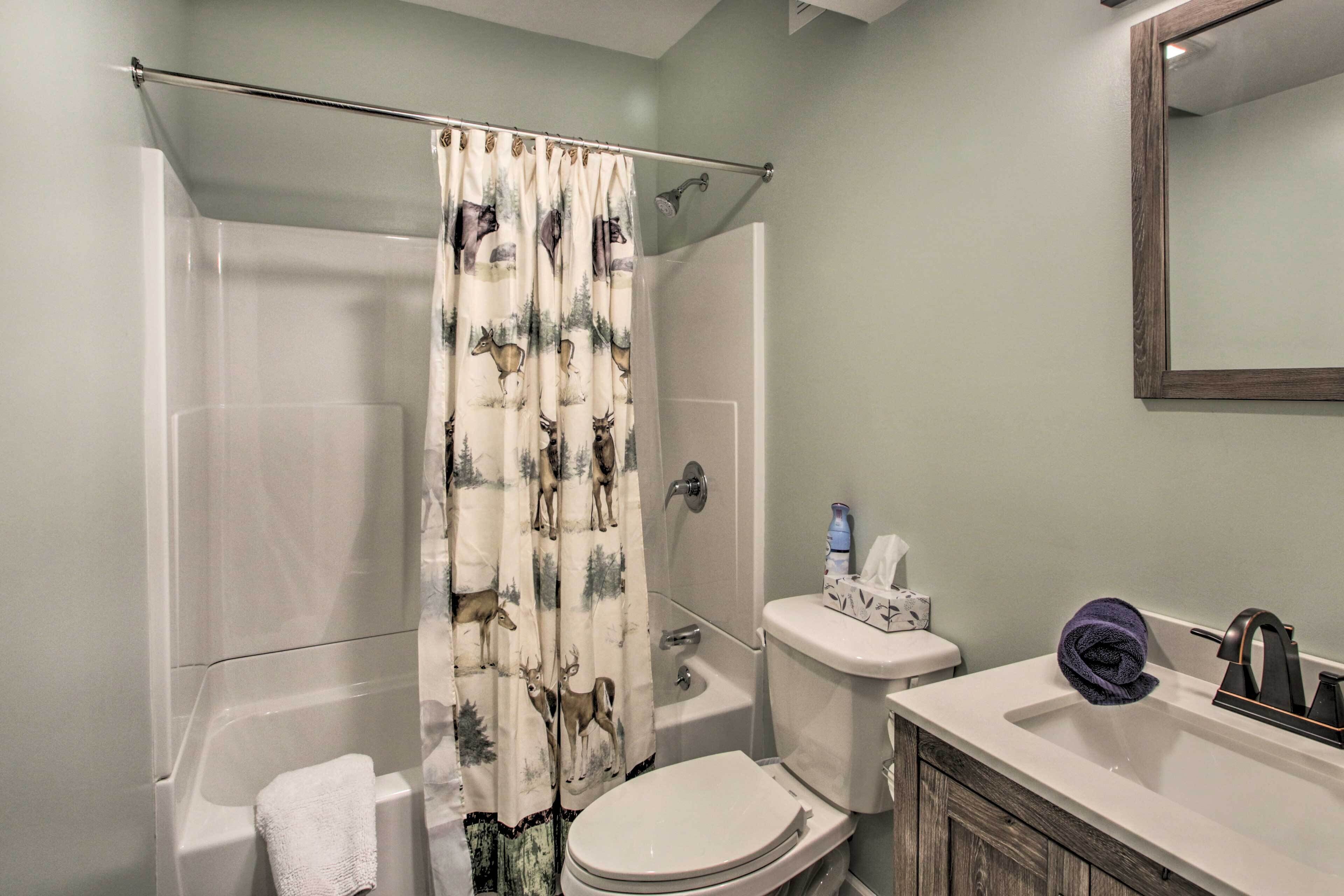 A bathroom with a shower curtain featuring deer prints, a toilet, a sink with a towel, and a mirror.