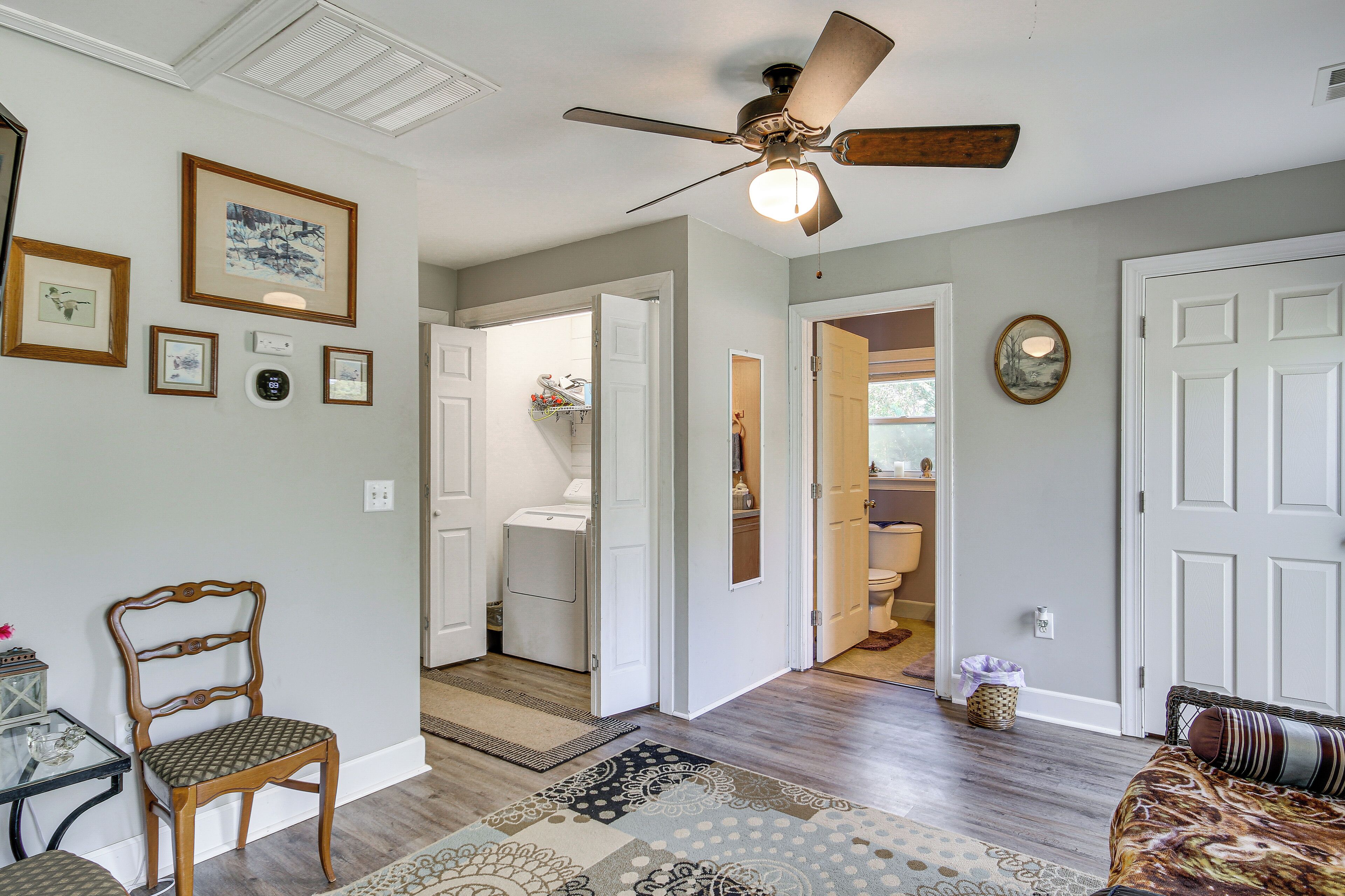 A room with a ceiling fan, a patterned rug, a wooden chair, and a bed with a patterned bedspread.