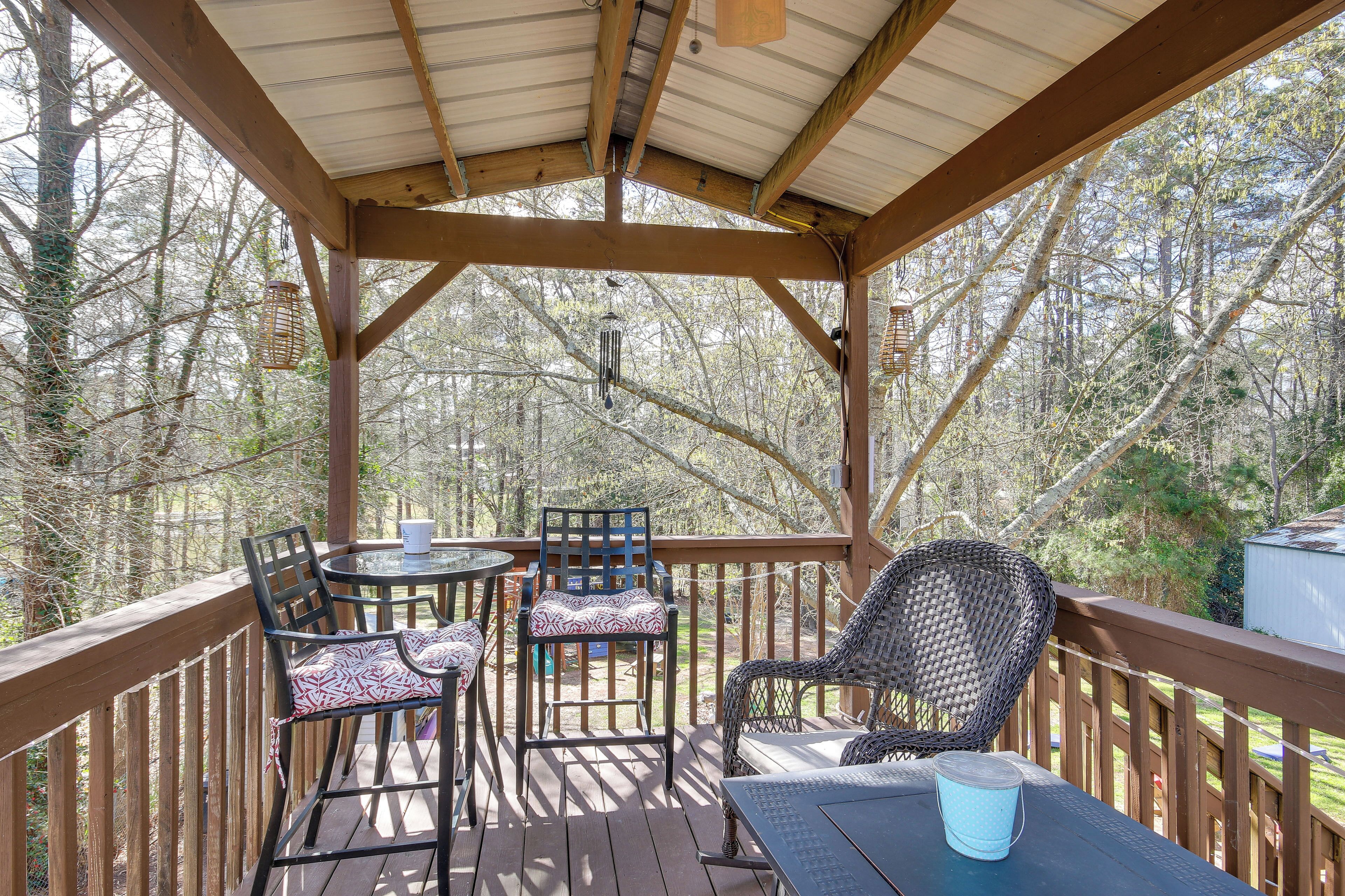 A covered outdoor deck with wooden railings, a table, two chairs, and hanging lanterns.