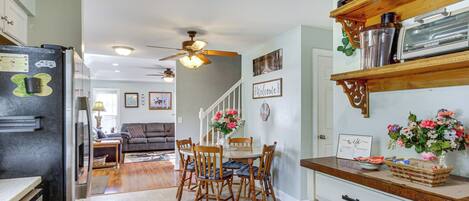 Une cuisine avec un coin repas, des chaises en bois, un réfrigérateur et un ventilateur de plafond.