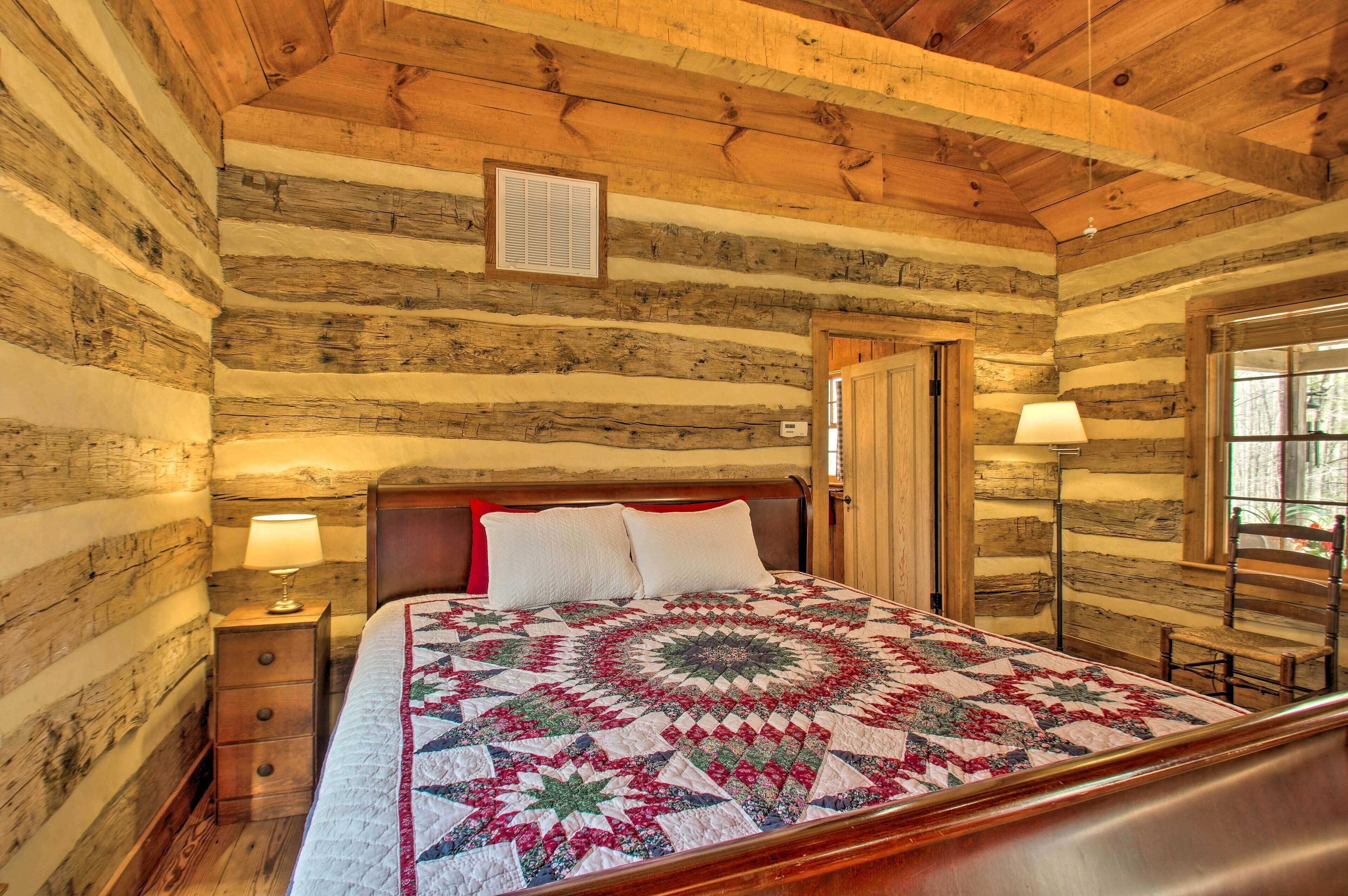 A log cabin bedroom with a bed, a nightstand, a lamp, and a window.