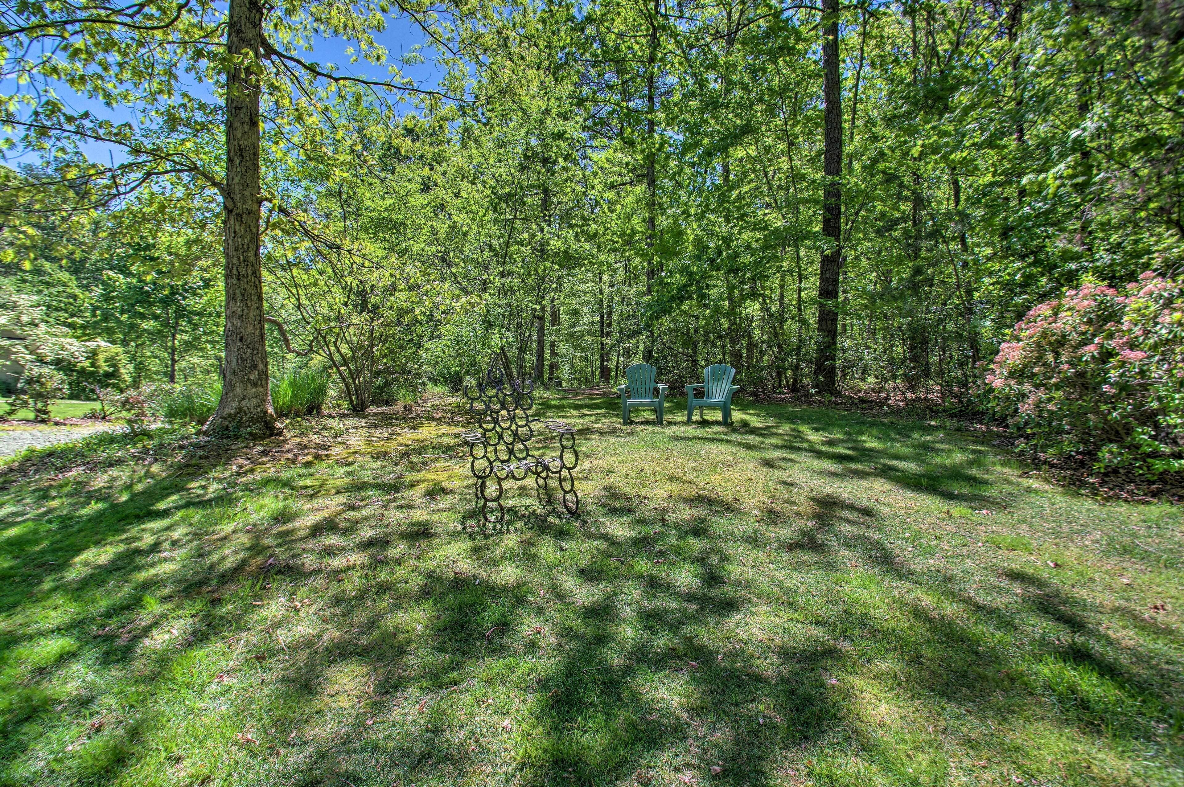 A wooded area with green chairs and a metal sculpture.