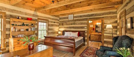 Interno di una baita di legno con un letto di legno, una scrivania, una sedia e un camino.
