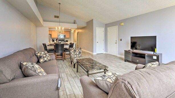 A spacious living room with a sofa set, a coffee table, and a TV. A dining area with chairs and a table is visible in the background. - Laguna Bay Resort Condo ~ 8 Mi to Disney! (Kissimmee)
