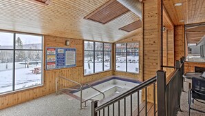 Ein Holzinnenraum mit großen Fenstern, einer Whirlpool-Badewanne und einer Treppe.