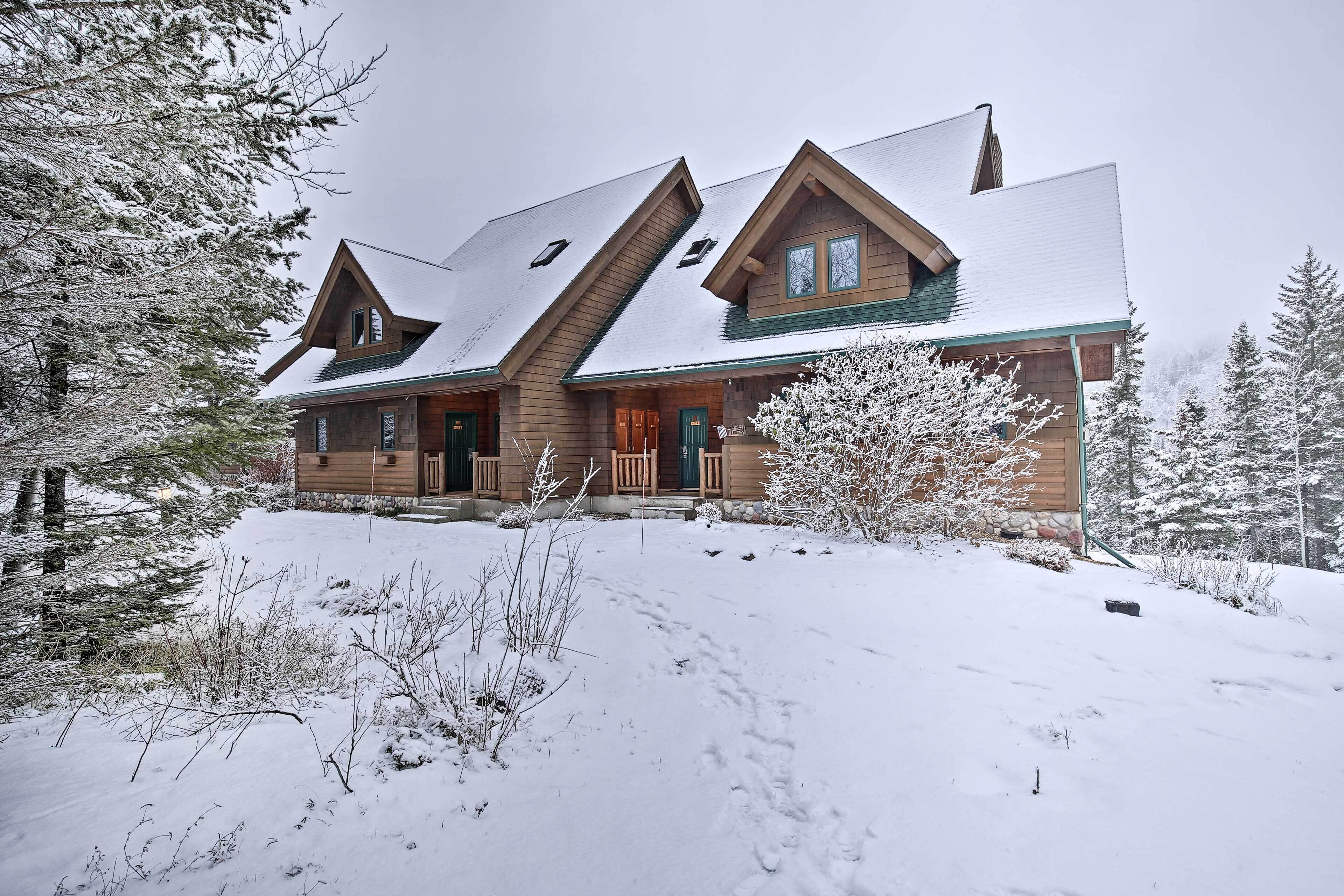 Une cabane en rondins avec un toit à forte pente, de nombreuses fenêtres et une véranda à l’avant.