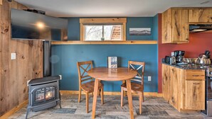 A cozy kitchen with a wood stove, wooden chairs, and a dining table. - Slopeside Burke Mountain Condo w/ Fireplace! (East Burke)