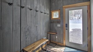 A wooden interior with a bench, coat hooks, a small table, and a door leading to a snowy outdoor area. - Slopeside Burke Mountain Condo w/ Fireplace! (East Burke)
