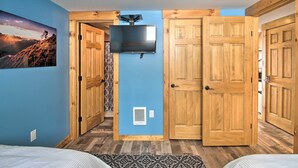A bedroom with a TV mounted on the wall, wooden doors, a patterned rug, and a mountain landscape painting. - Slopeside Burke Mountain Condo w/ Fireplace! (East Burke)