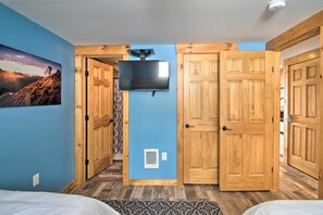 A bedroom with a TV mounted on the wall, wooden doors, a patterned rug, and a mountain landscape painting. - Slopeside Burke Mountain Condo w/ Fireplace! (East Burke)