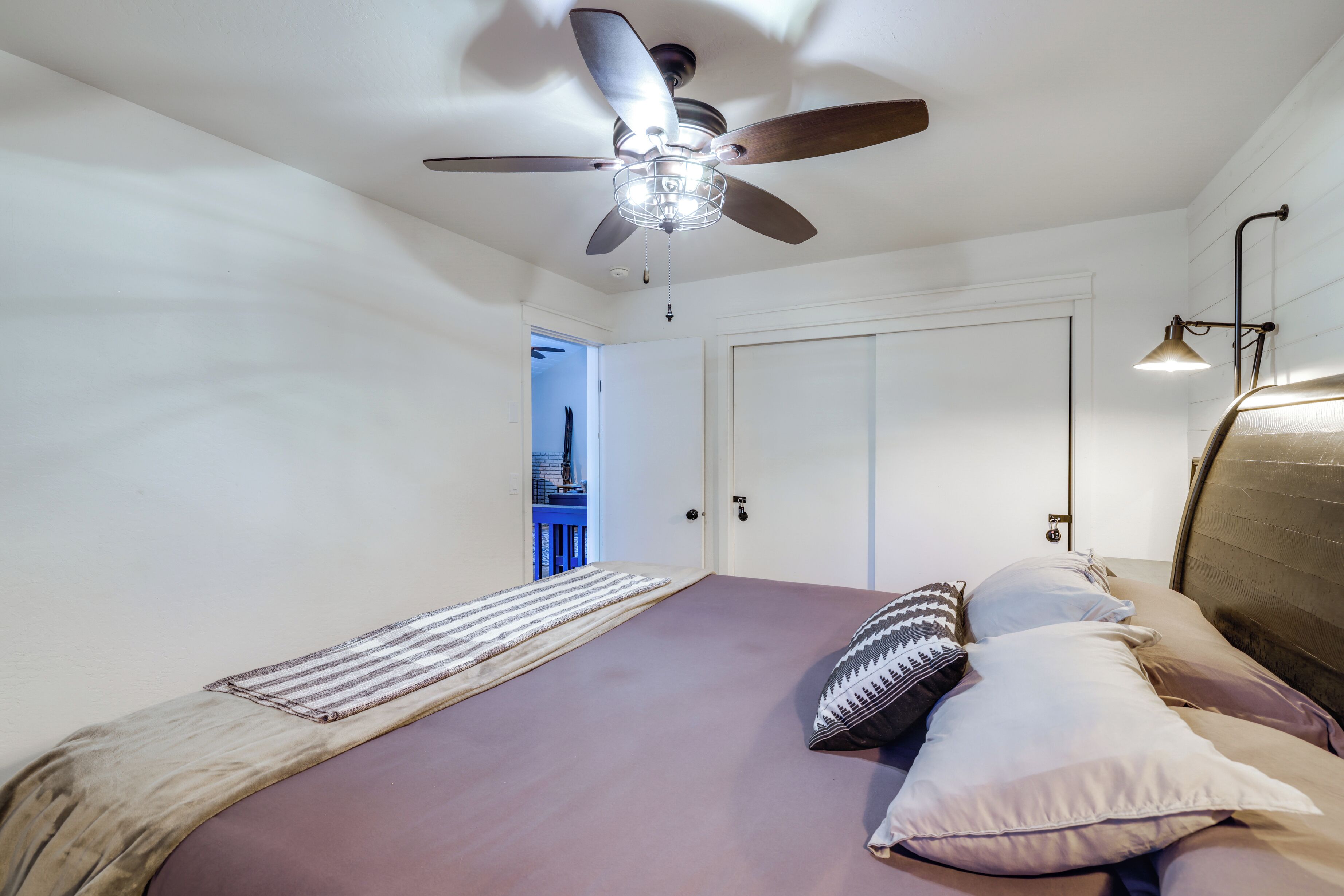 A bedroom with a bed, a ceiling fan, a door, and a nightstand.