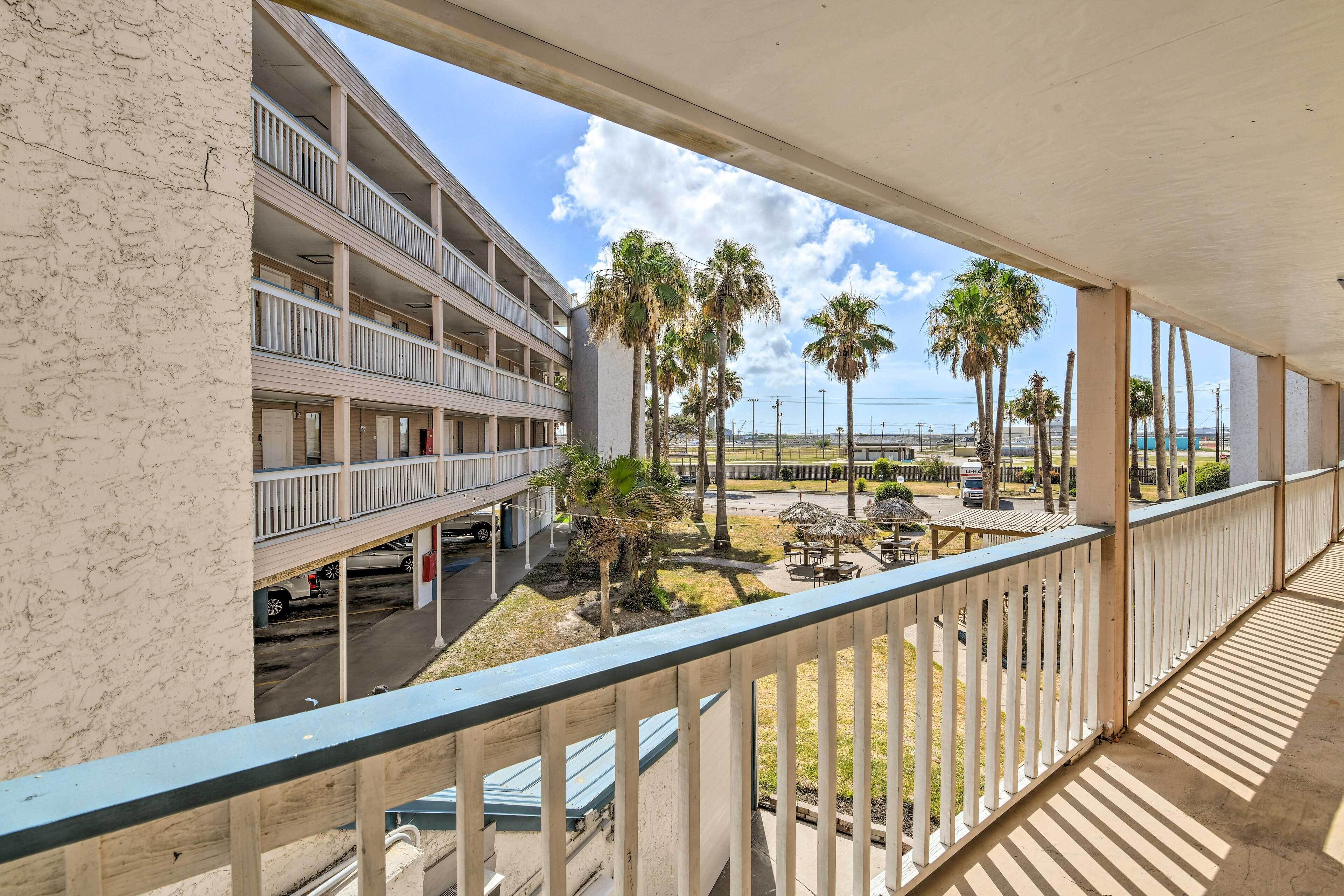 A multi-story hotel with balconies overlooking a parking area and a beach with palm trees.