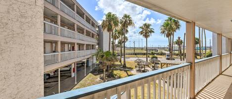 A multi-story hotel with balconies overlooking a parking area and a beach with palm trees.