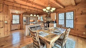 A wooden cabin interior with a dining area, kitchen, and large windows. - Decks & Mountain Views: Waynesville Getaway! (Waynesville)