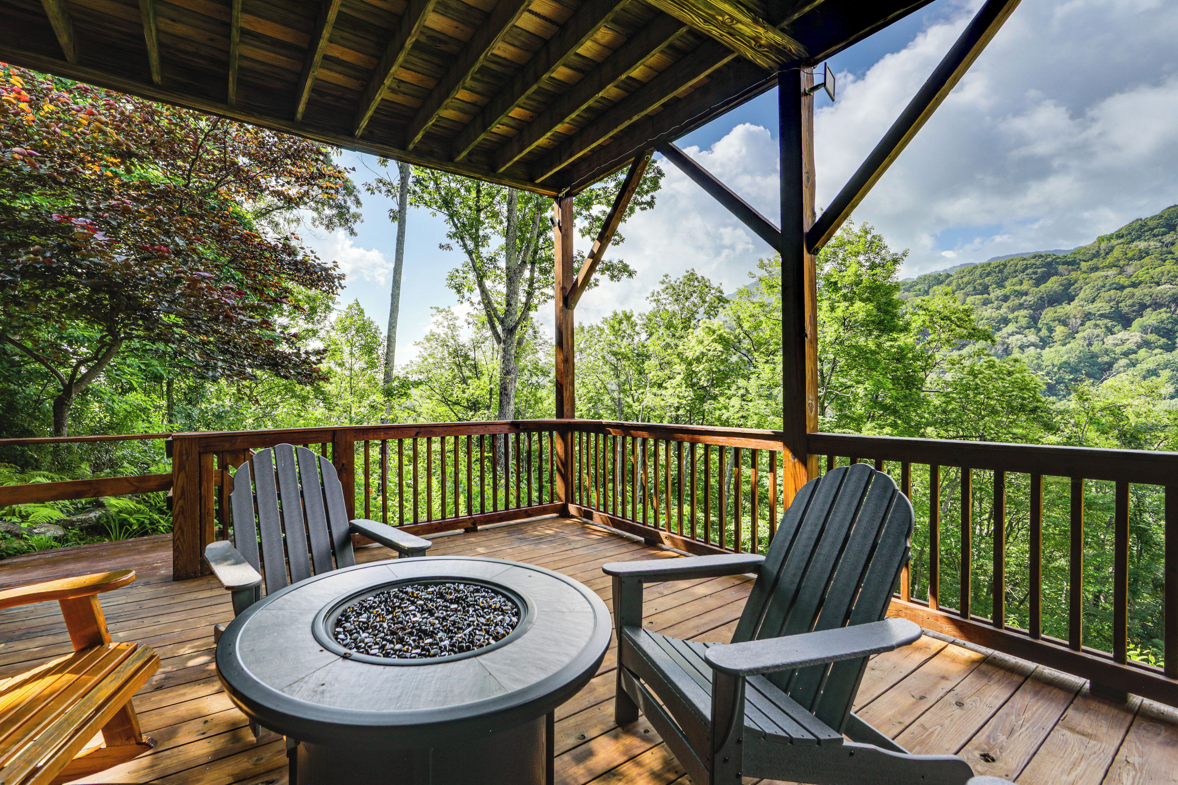 Eine Holzterrasse mit Adirondack-Stühlen und einem runden Tisch mit einem Feuerkorb.