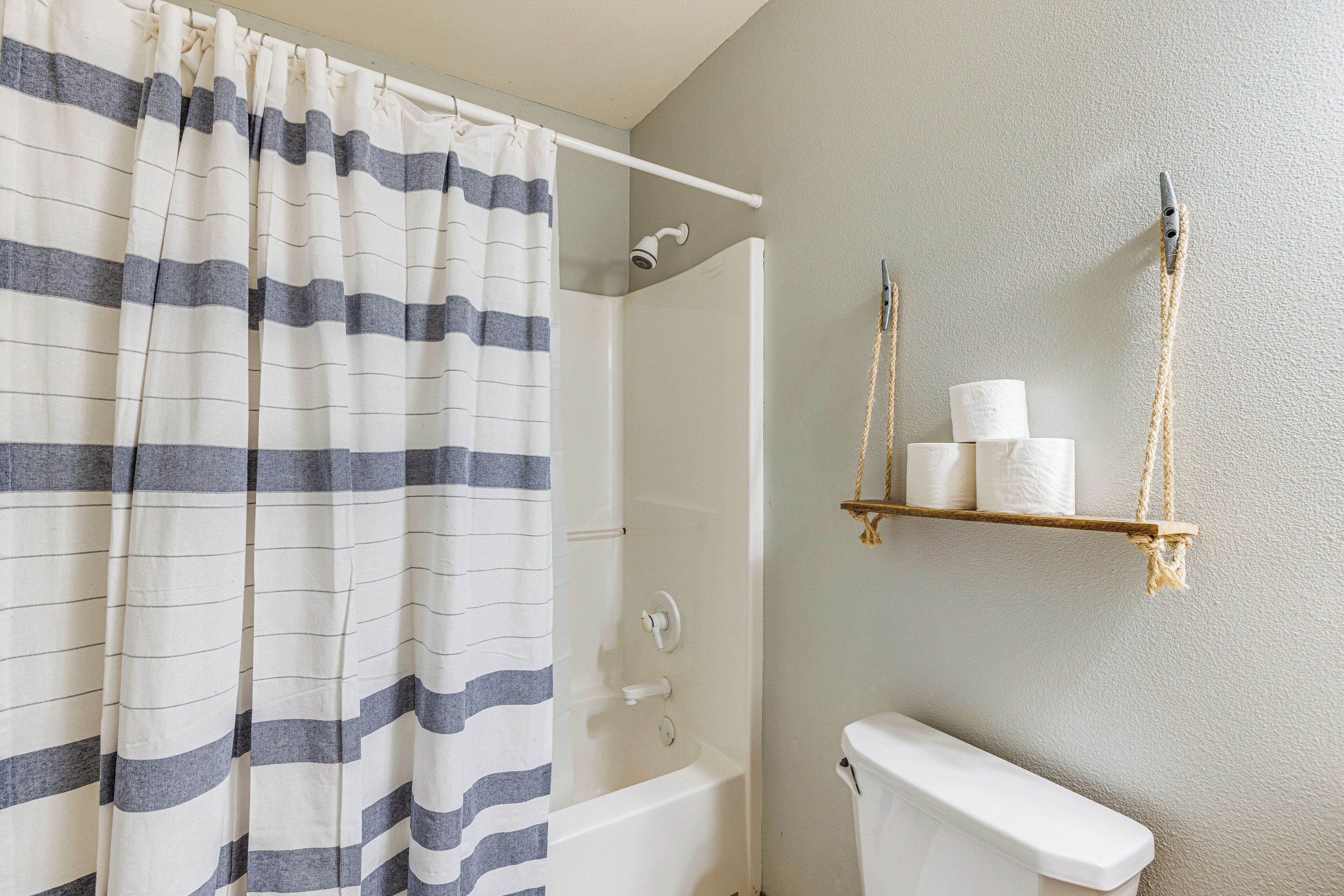 Ein Badezimmer mit Duschvorhang, Badewanne, Toilette und Ablage für Toilettenpapier.