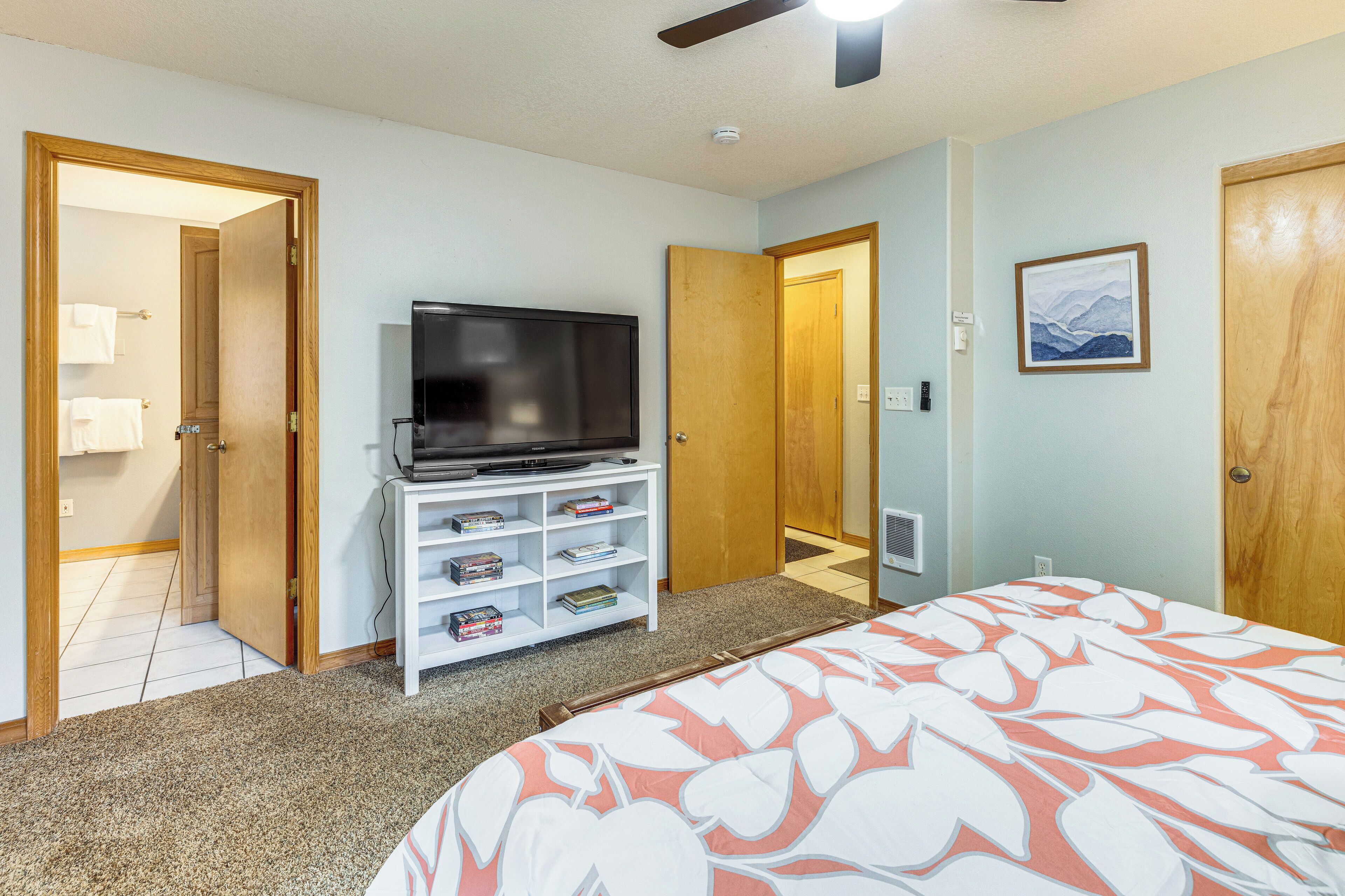 A bedroom with a bed, a TV on a stand, a bookshelf, and two doors.