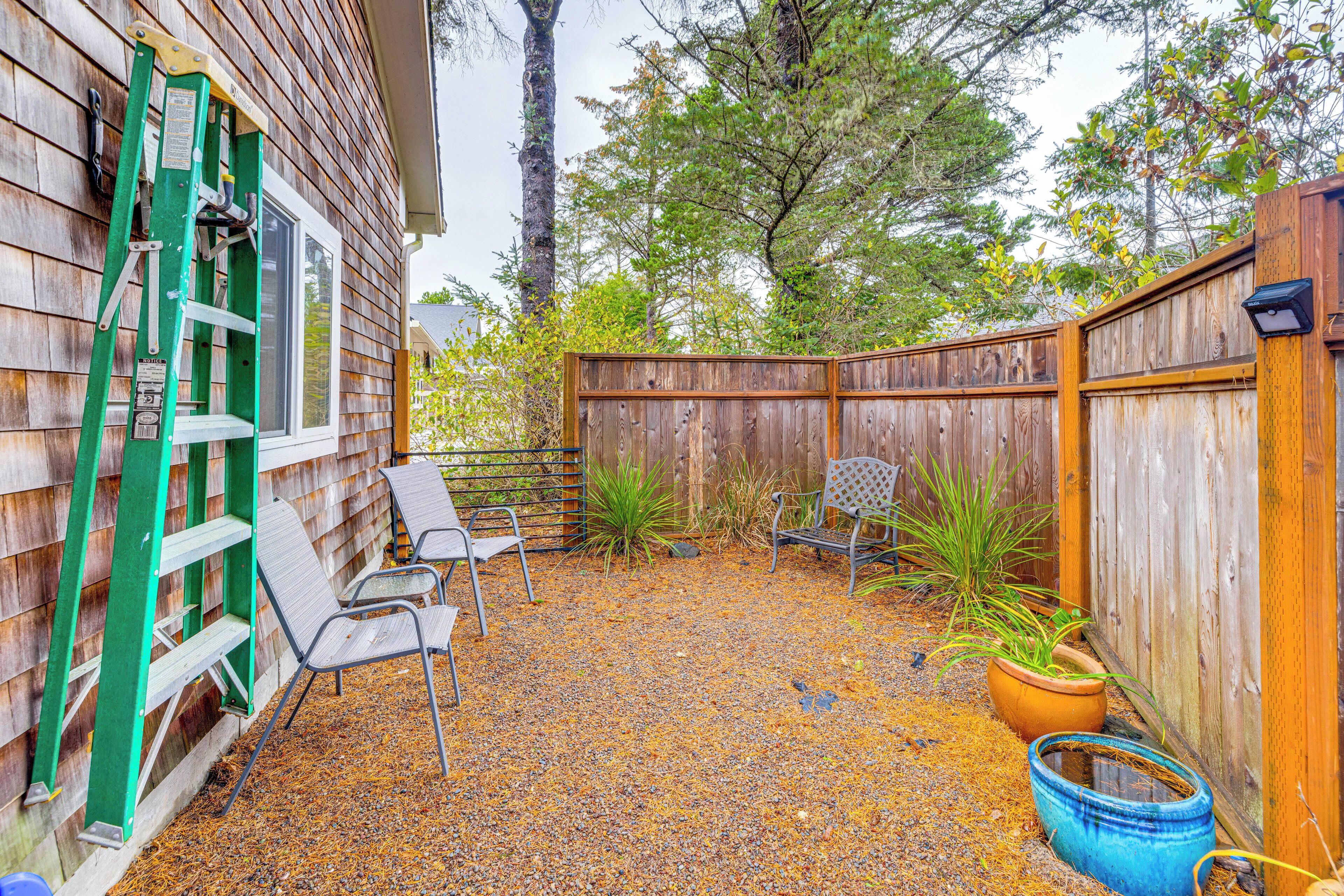 Un patio trasero con cerco de madera, escalera verde, sillas de metal y una planta en maceta.