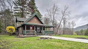 A log cabin with a green porch and a red door, surrounded by a grassy yard and trees. - Lovely Fort Ann Lodge - 10 Mi to Lake George! (Fort Ann)