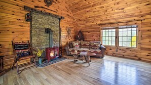 A log cabin interior with a stone fireplace, wooden walls, a leather sofa, and a large window. - Lovely Fort Ann Lodge - 10 Mi to Lake George! (Fort Ann)
