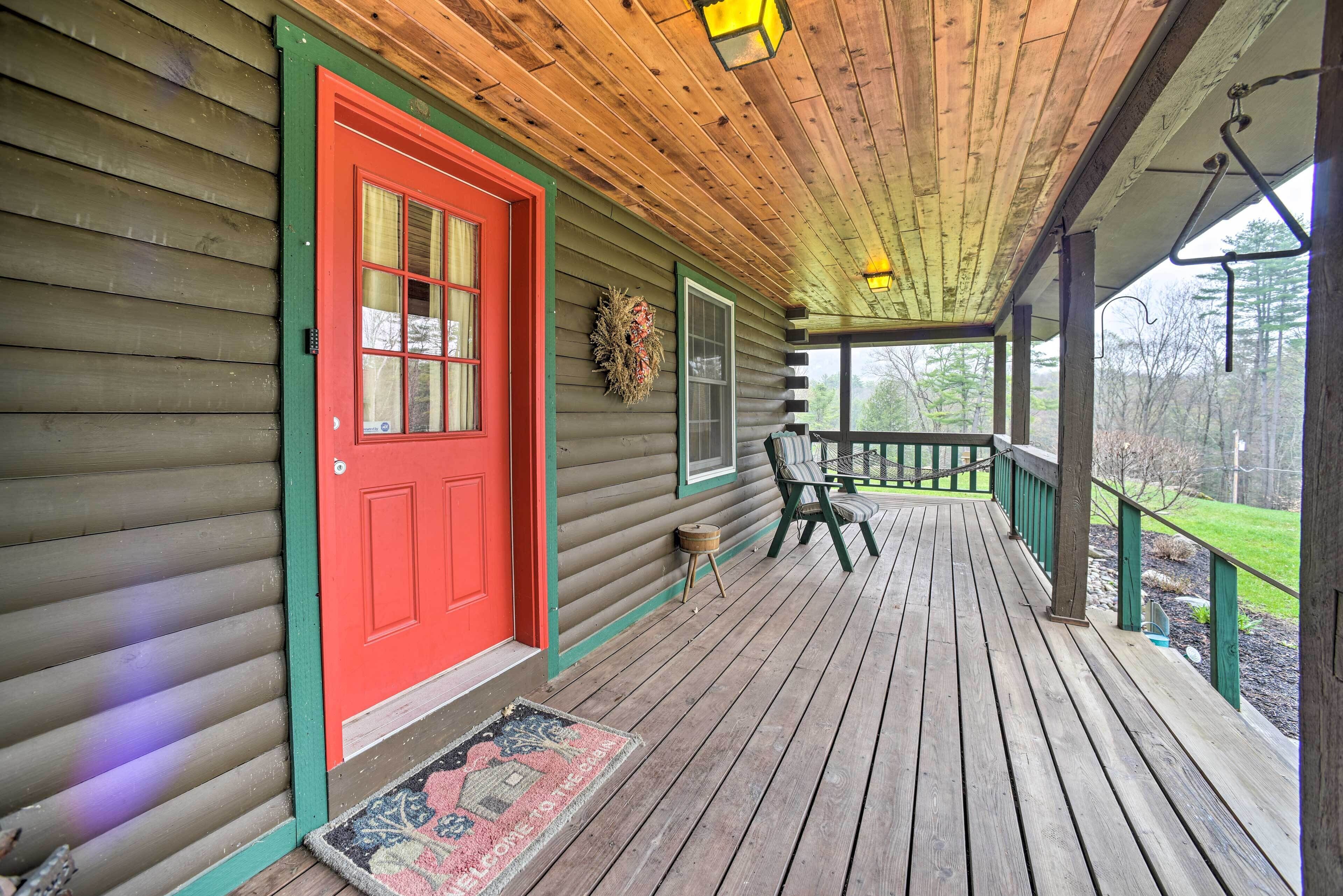 A wooden porch with a red door, a small table, and a chair.