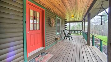 A wooden porch with a red door, a small table, and a chair.