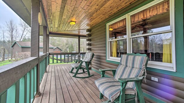 A wooden porch with rocking chairs and a view of the surrounding area. - Lovely Fort Ann Lodge - 10 Mi to Lake George! (Fort Ann)