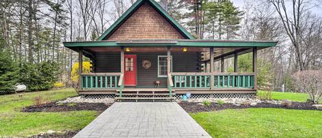 A log cabin with a green porch and a red door, surrounded by a landscaped garden and trees.