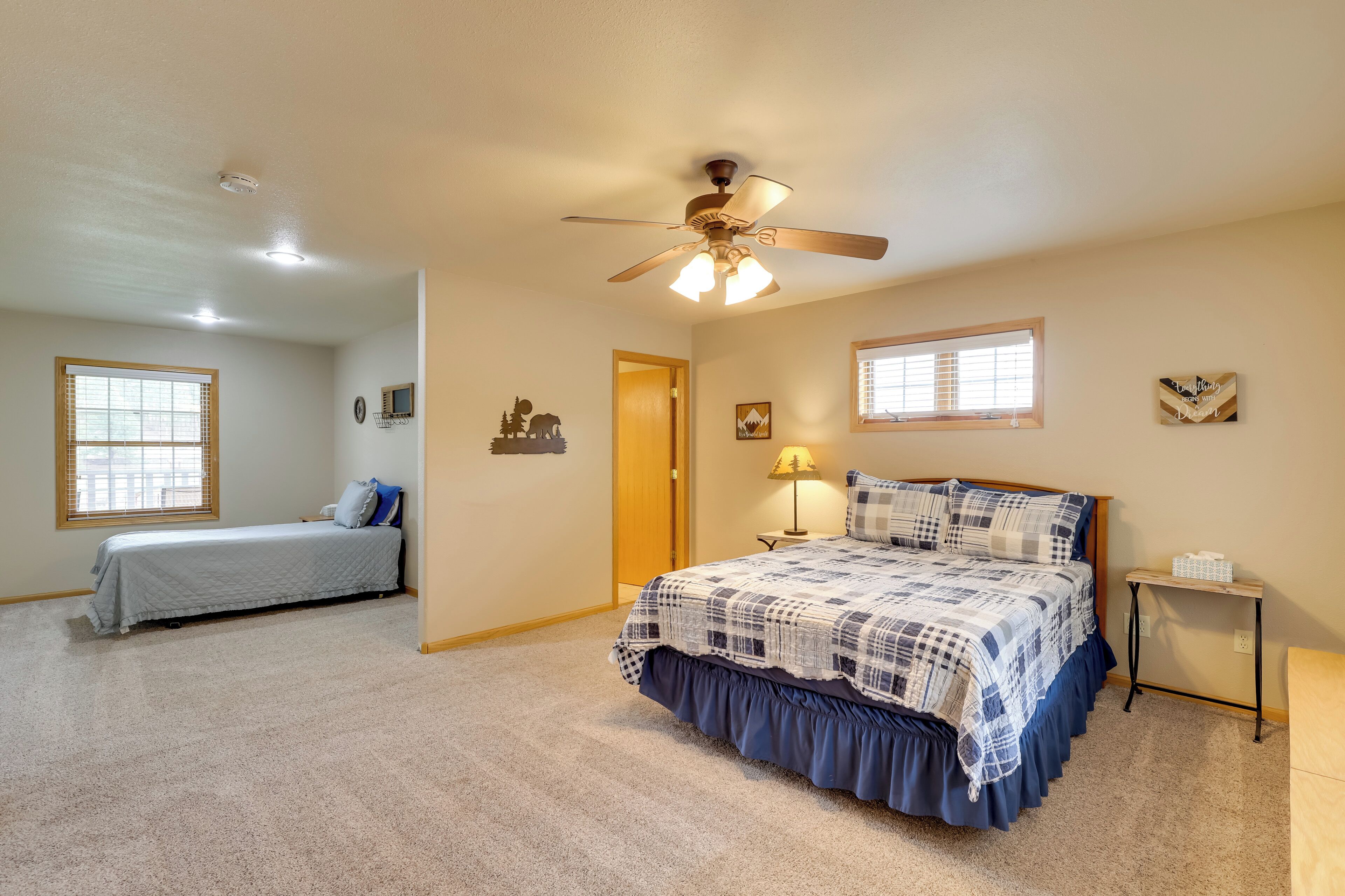 A bedroom with a large bed, a smaller bed, a ceiling fan, and a window.