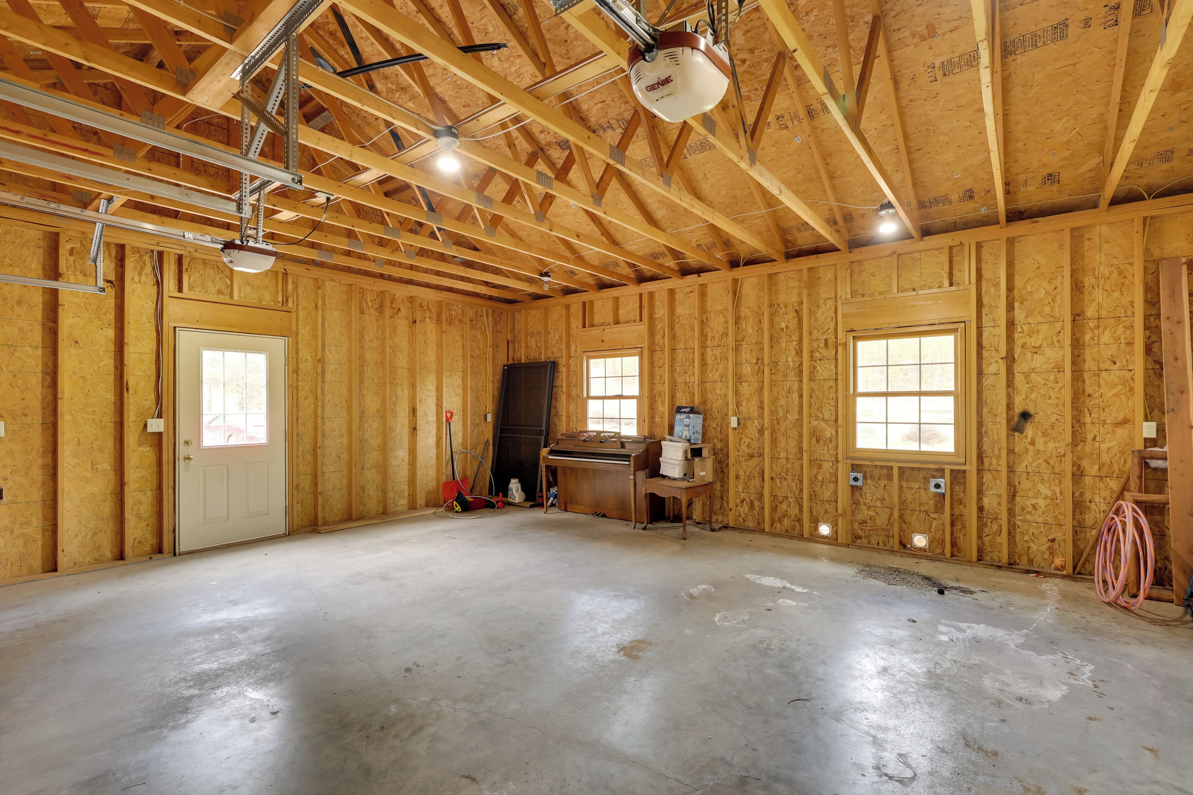 A room with exposed wooden beams, a door, a window, and a workbench.