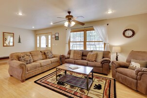 A living room with two sofas, a coffee table, a ceiling fan, and a large window with curtains.