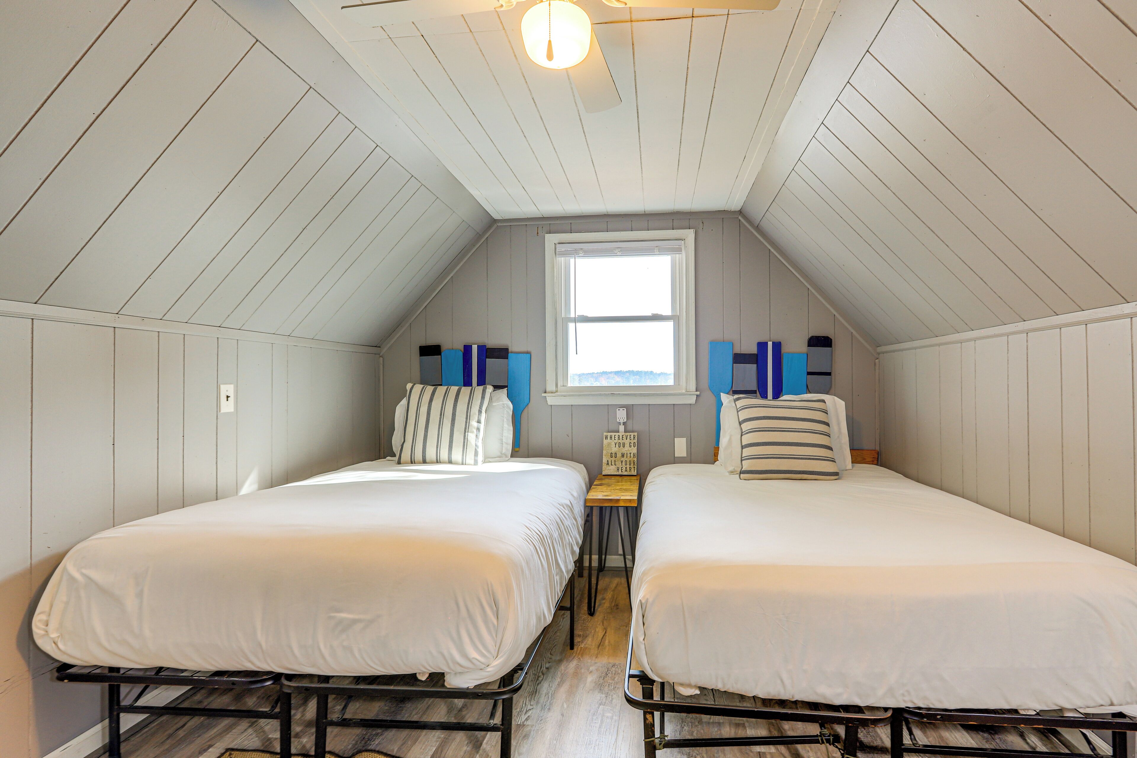 A small, cozy attic bedroom with two beds, a window, and a wooden floor.