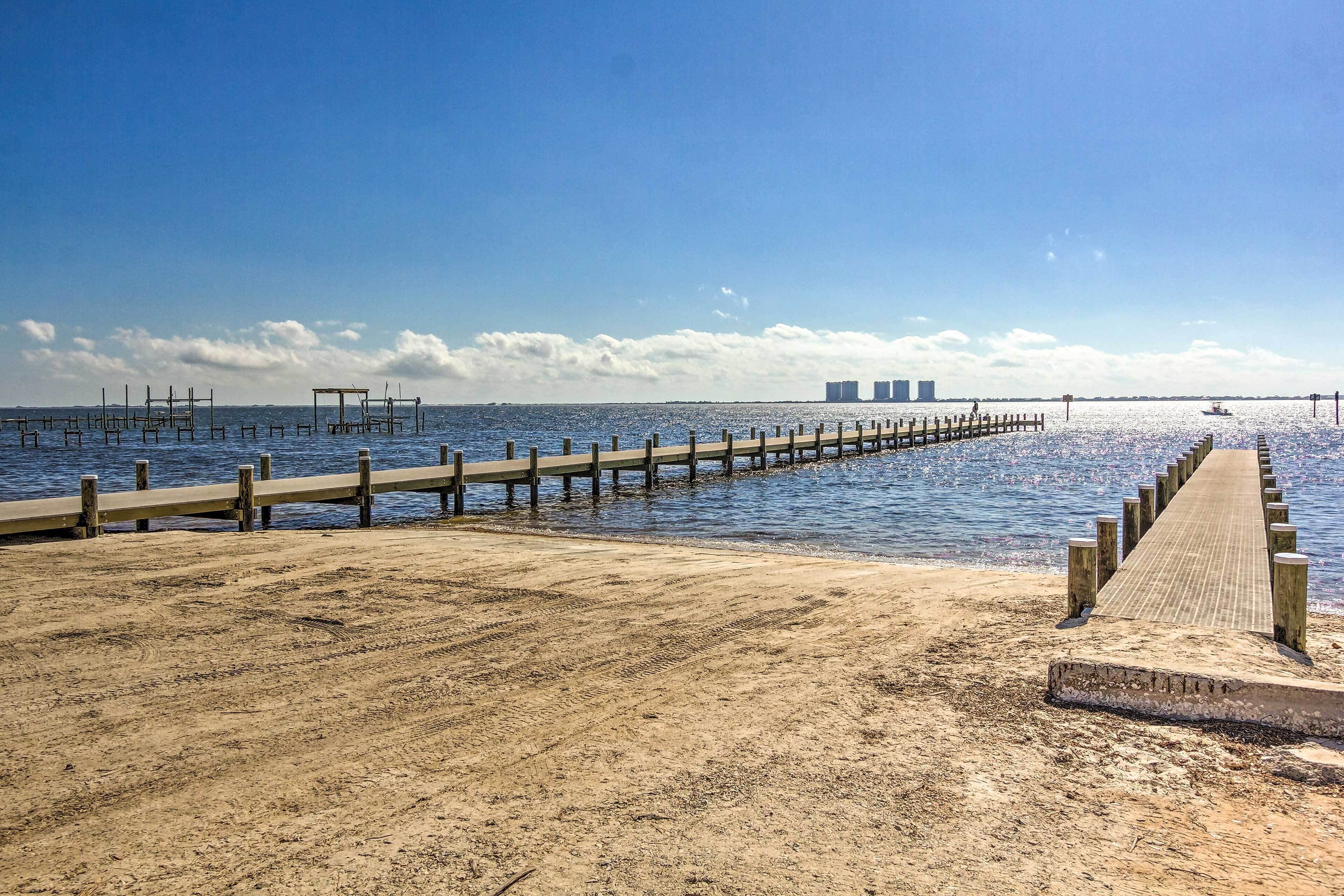 A sandy beach with a wooden pier extending into the water, leading to a dock.