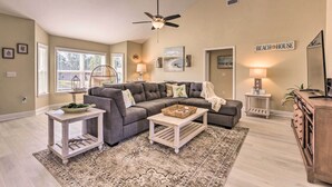 A living room with a gray sectional sofa, a wooden coffee table, a standing lamp, and a ceiling fan.