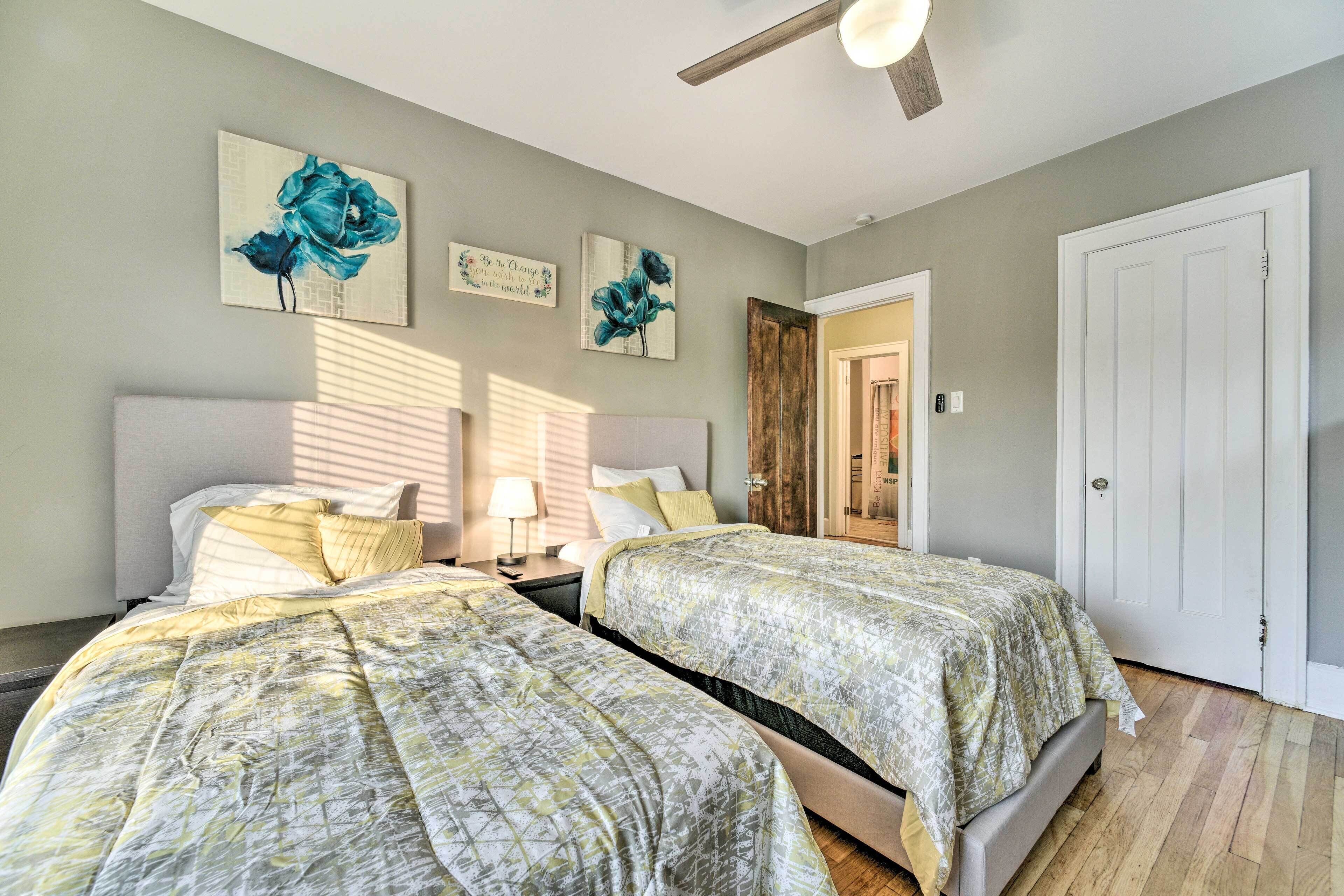 A bedroom with two beds, a ceiling fan, and artwork on the walls.