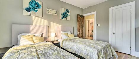 A bedroom with two beds, a ceiling fan, and artwork on the walls.