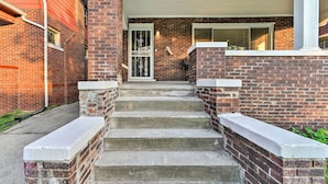 A set of concrete steps leading to a door with a glass panel, flanked by brick walls and a white overhang. - Elegant Detroit Home w/ Yard ~ 5 Mi to Dtwn! (Detroit)