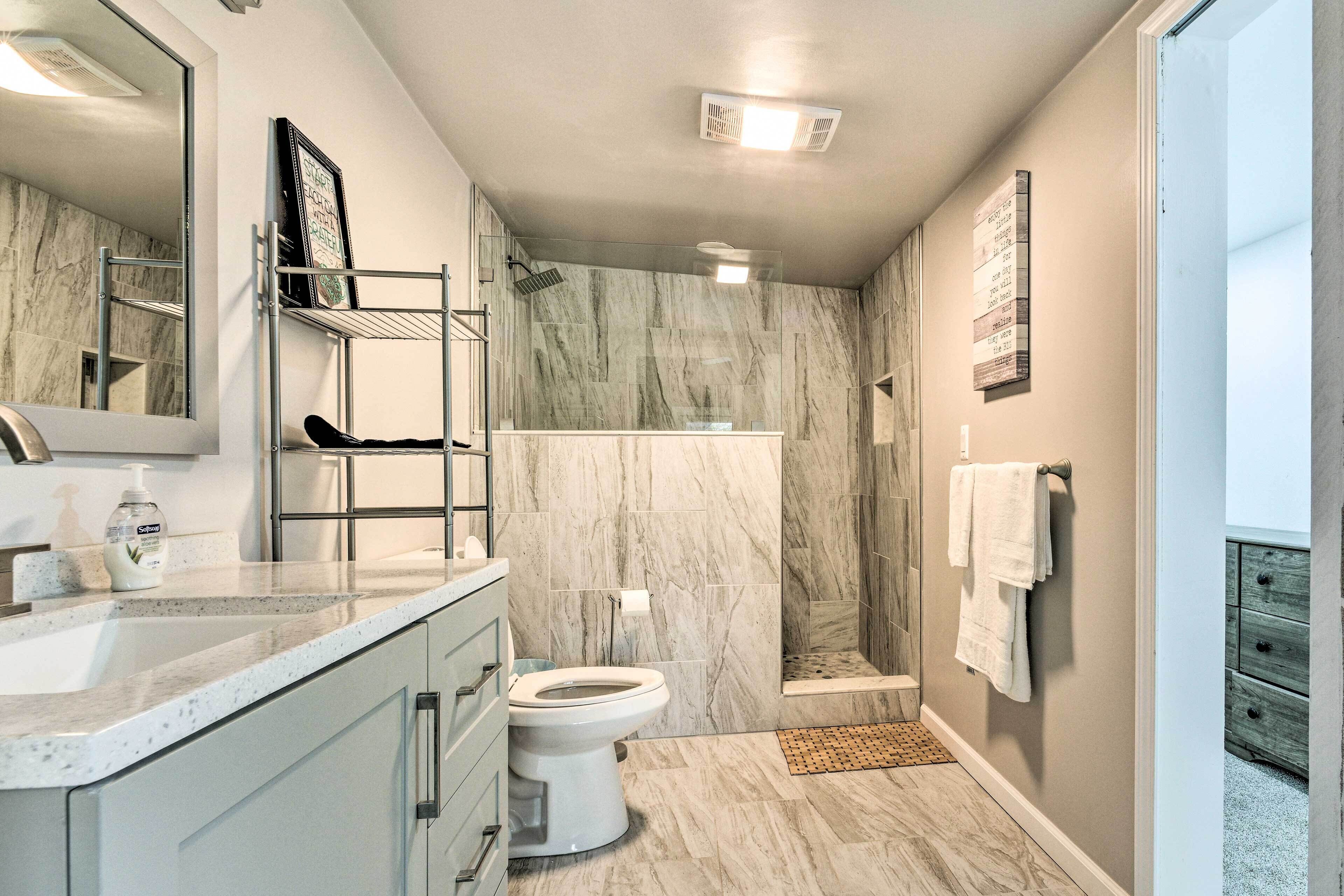 Une salle de bain avec une douche en marbre, des toilettes, un lavabo avec un miroir et un porte-serviettes.