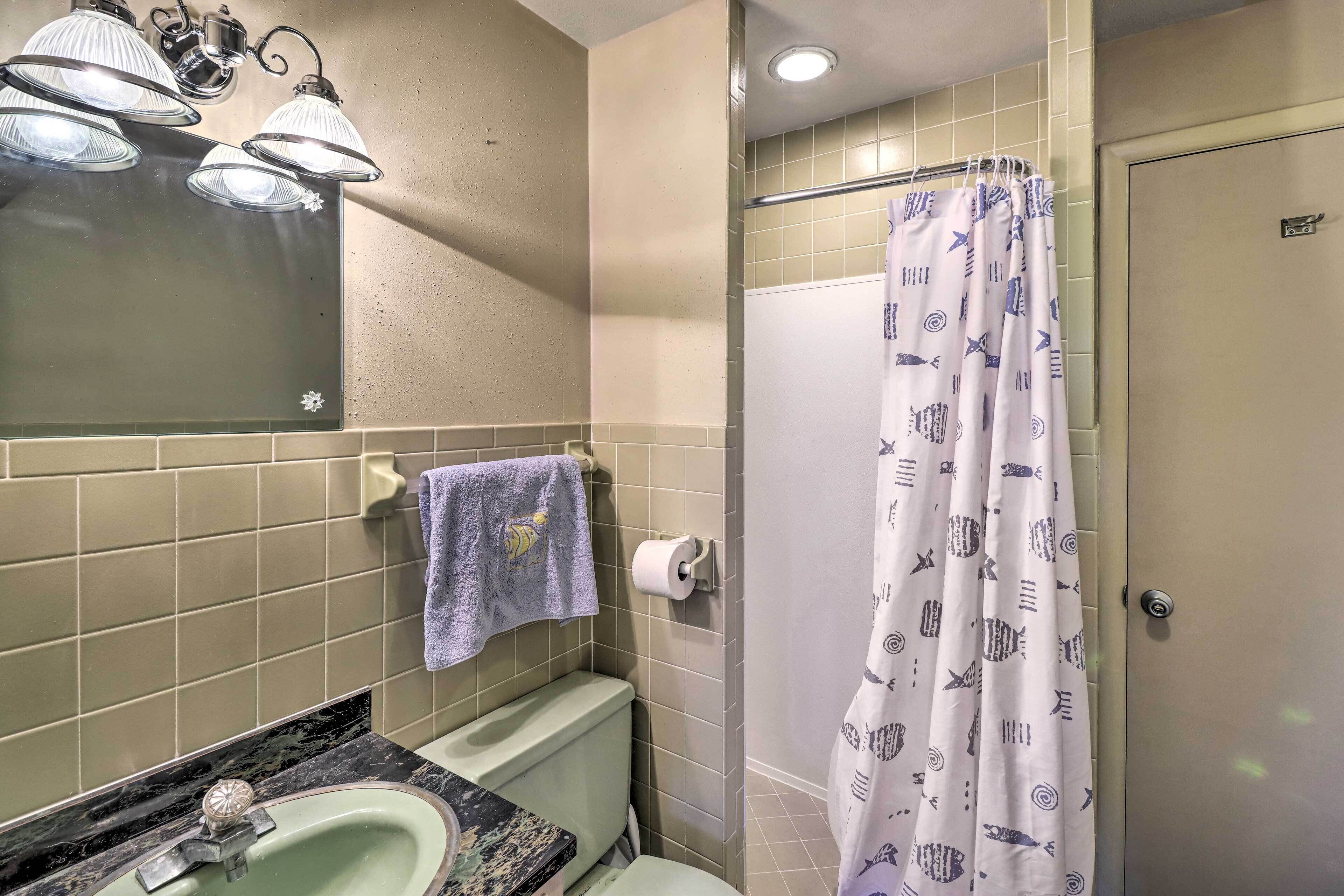 A bathroom with a sink, mirror, towel rack, toilet, shower curtain, and a towel hanging on the wall.